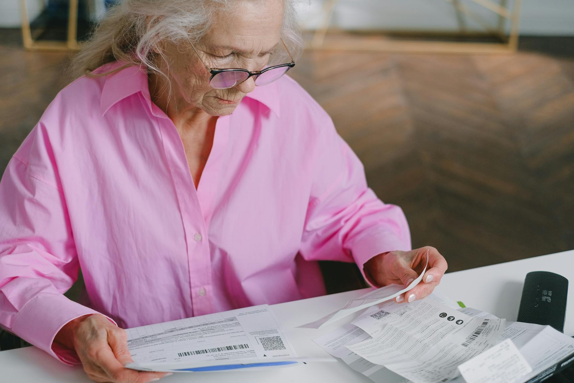 An Elderly Woman in Pink Long Sleeves Sitting while Reading Documents
