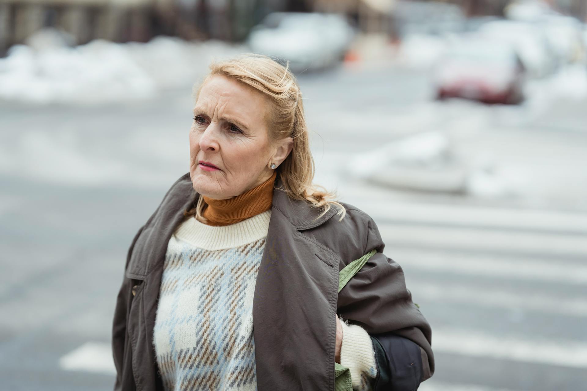 Thoughtful elderly woman in outerwear on city roadway